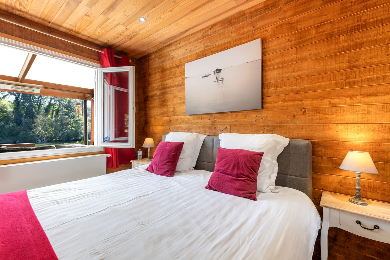 Large bed in the wood bedroom, red cushions and a picture