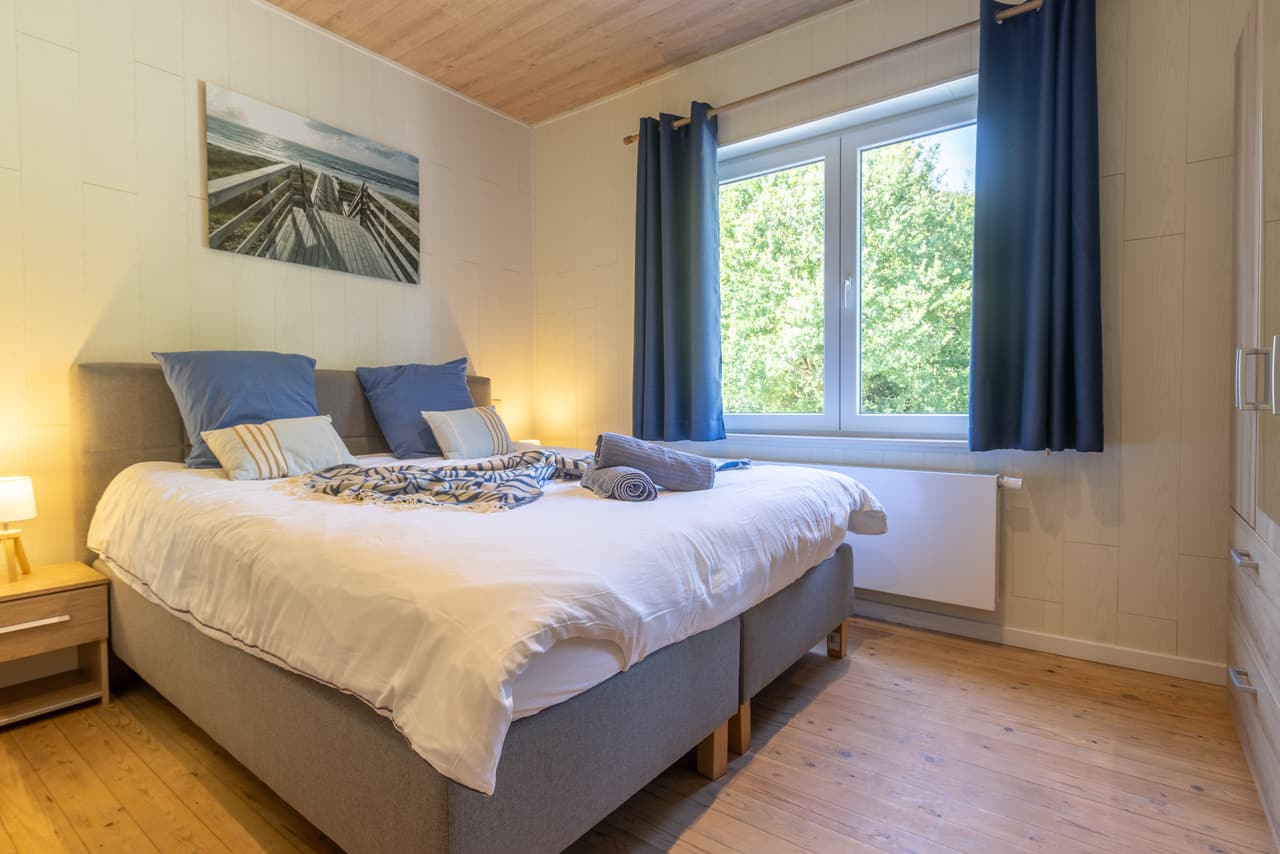 Bedroom with blue curtains, a large bed and a window onto the greenery