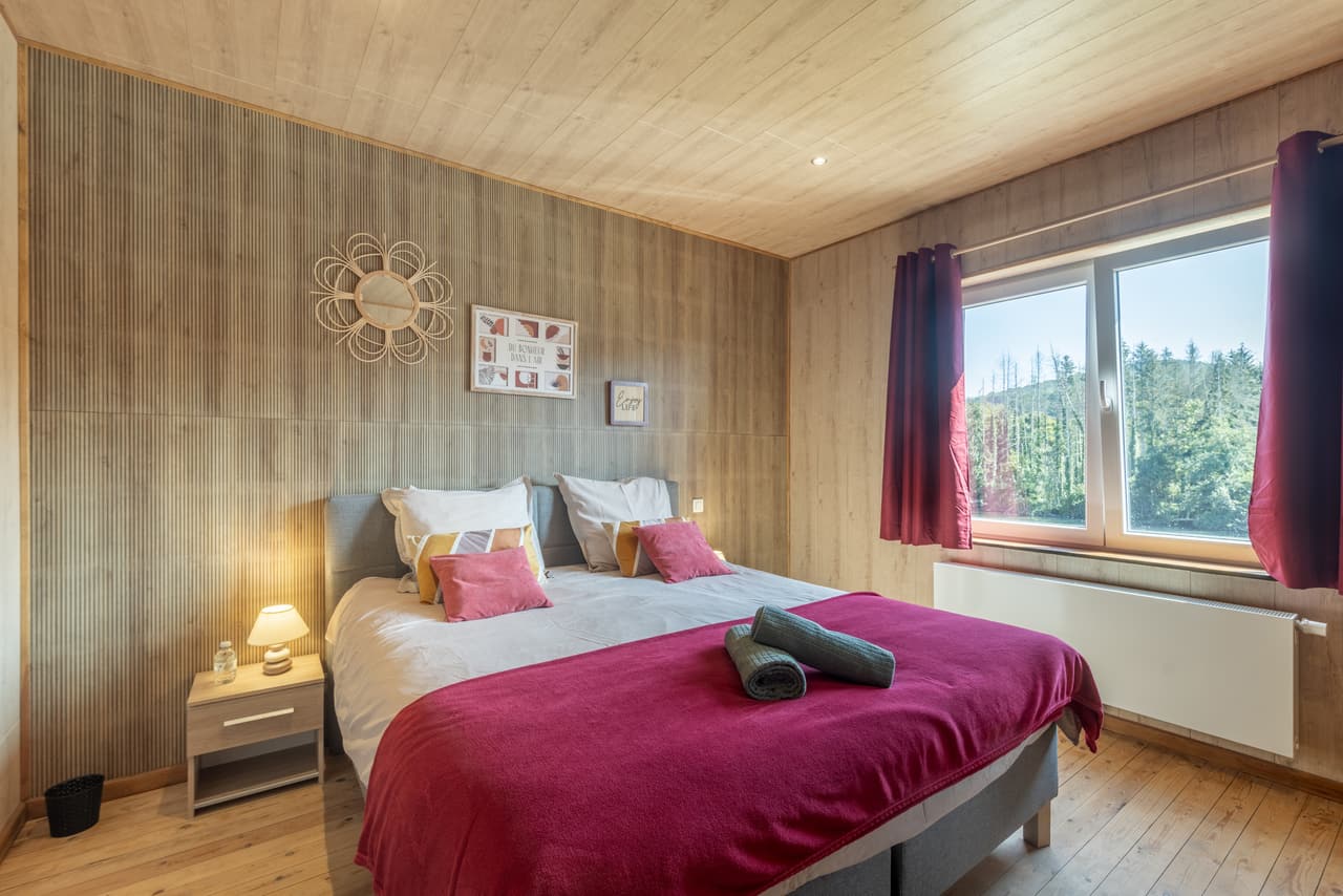 Wood-panelled bedroom with a raspberry throw and a window onto the forest