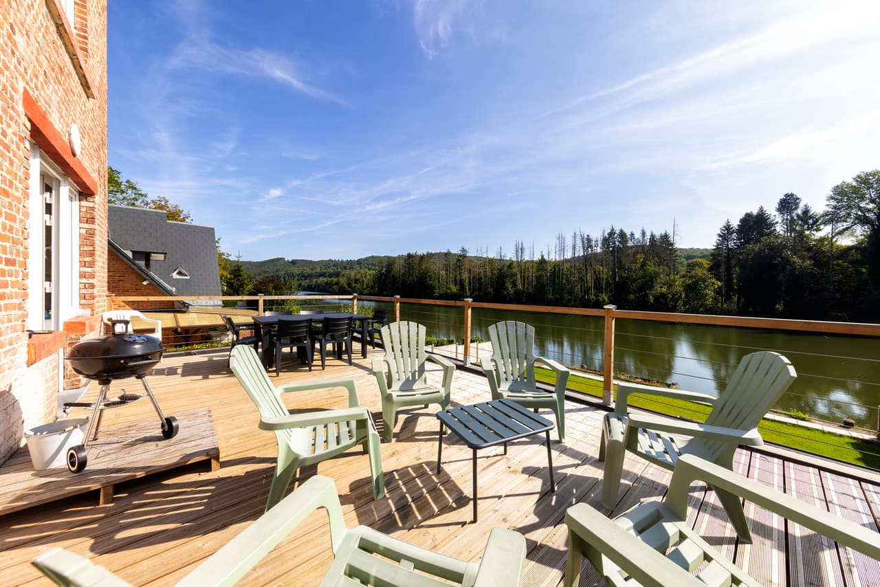 Wooden terrace with Adirondack chairs, a barbecue and a view of the Meuse